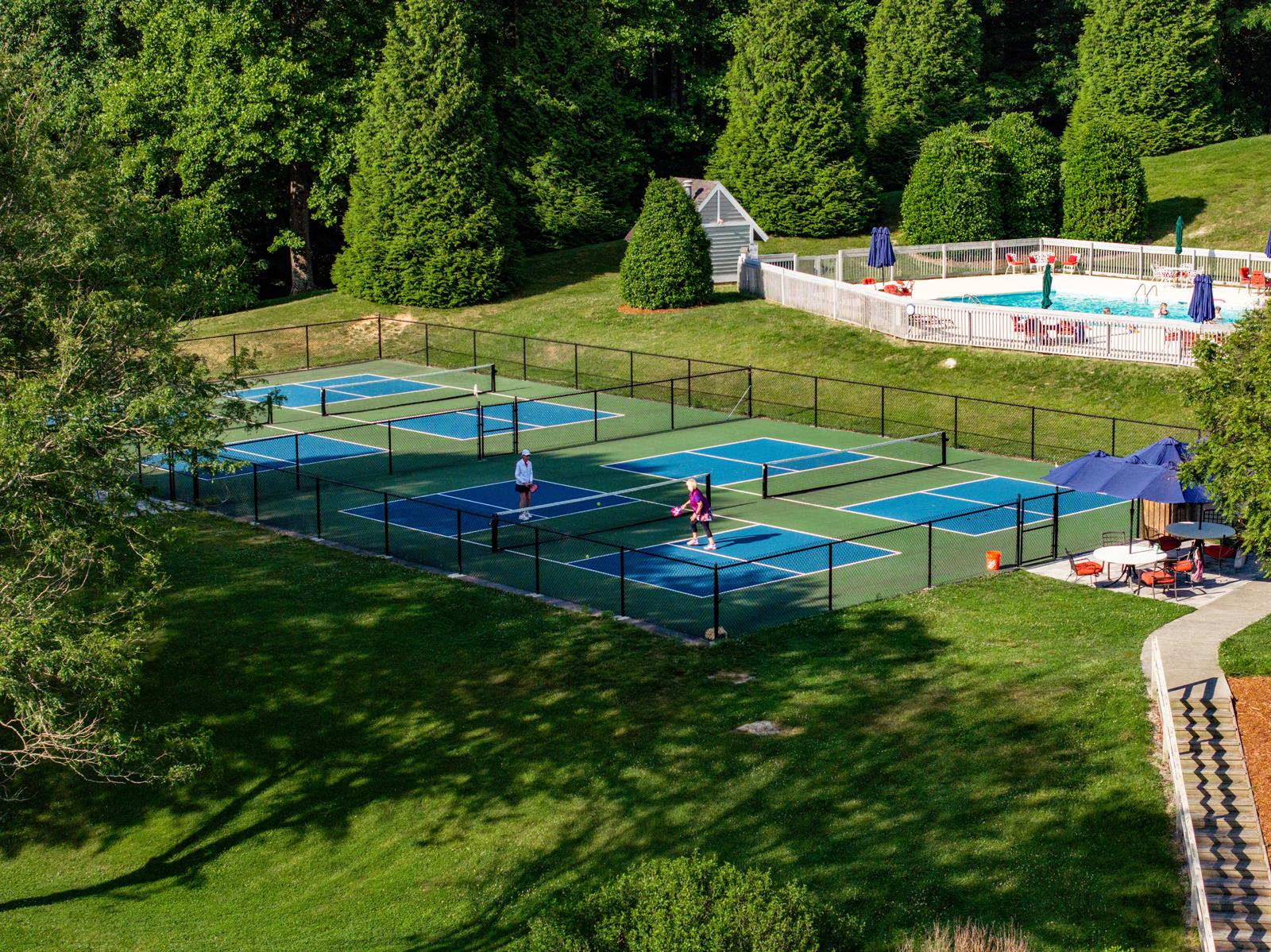 Pickleball court and pool surrounded by trees at Kenmure Country Club, showcasing amenities in a natural setting.
